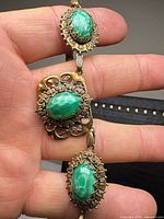 Close-up of two necklace stations showing brass filigree and mottled green glass cabochons
