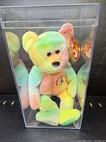 Front view of tie-dye Peace bear inside acrylic case showing swing tag and peace symbol