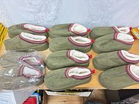 All six pairs of green suede clog slippers on tabletop, one pair bagged