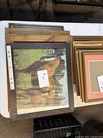 Stack of wooden frames on table showing horse print and additional frames beneath