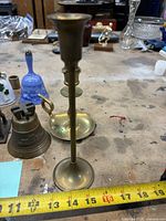 Group shot showing tall brass candlestick, shorter candlestick, three bells, Liberty Bell plaque bell on workbench