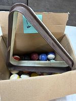 Brown plastic triangle rack resting on assorted multicolor billiard balls in cardboard box