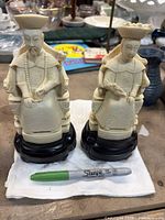 Front view of both figurines on bases with size reference Sharpie