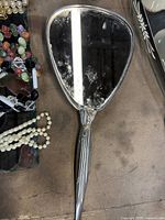 Silver-plated hand mirror with tarnish, faux pearl necklaces and beaded jewelry visible