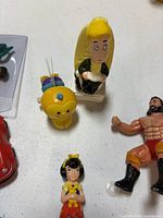 Group of assorted small toys showing yellow bug, blonde figure, wrestler and partial red McDonald's car