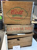 Front view of all three wooden beverage crates stacked, showing Cott and Canada Dry branding and overall wear
