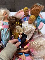 Group of dolls showing multiple Barbie-style figures, two Ken dolls and child-size doll