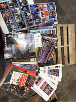 Stack of mixed sports magazines and visible uncut trading card sheets on pallet