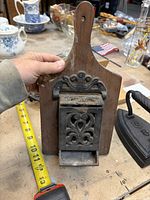 wood backboard match safe with cast iron front and flat iron beside for scale