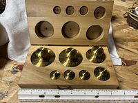 Open box showing seven brass weights seated in recesses with visible stamped denominations