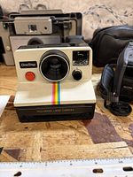 Front view of Polaroid OneStep camera with accessories visible in background