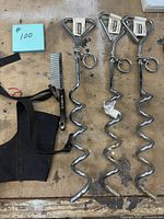 Three chrome spiral ground anchors, black muzzle, metal comb on workbench