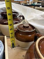 Brown and tan stoneware crock with lid beside tape measure