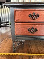 front view showing red drawers, black frame, metal pull handles, scrolled metal leg