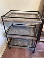 Front angled view of three-tier bar cart showing shelves, metal frame and casters