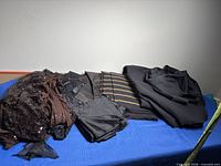 Overview of all fabric pieces laid on table: brown sequined fabric, assorted black fabrics, striped black and gold fabric