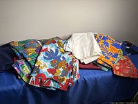 Group of assorted folded fabrics including solids, tropical prints, white cloth, and orange floral print