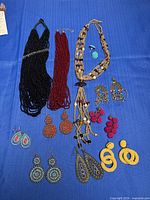 Group shot of all three necklaces and eight earring pairs laid out on blue background