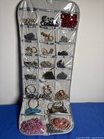 Front side of hanging organizer showing multiple pockets filled with assorted jewelry