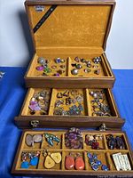 Open jewelry box showing multiple compartments with assorted costume rings and earrings