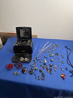 Overall view of black travel case open beside assortment of necklaces, earrings and brooches on blue surface
