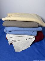 Stack of five folded knit fabrics in burgundy, grey, blue, taupe and cream