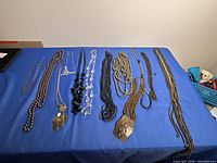 Overview of ten assorted necklaces laid out on blue surface