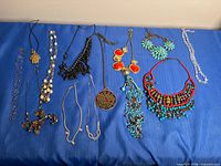 Overview of all twelve necklaces laid out on blue surface