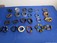 Full layout of twenty-four assorted stretch bracelets on blue surface