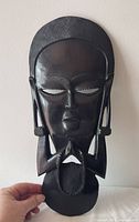 Front view of entire ebony wood mask showing facial details and prayer hands