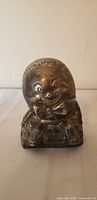 Front view of silver plated Humpty Dumpty coin bank showing figure and brick wall base