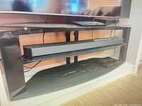 Front view of black metal and glass TV stand showing two shelves and overall form