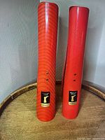 Front view of both red plastic boot shapers standing upright on wooden surface showing labels