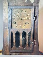 Front view of wood mantel clock with door closed showing dial, hands and lower cut-outs