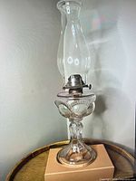 Full view of clear glass oil lamp with brass burner and chimney