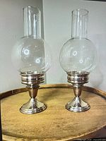 Both silver-plated candle holders with glass chimneys on tray