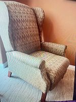 Full view of one wingback recliner showing upholstery, back, arms, legs