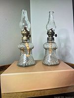 Front view of the two miniature oil lamps showing glass reservoirs, brass burners, chimneys and wicks