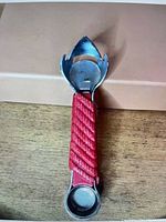 Full view of tool showing opener head and capper end with red rope handle