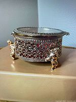 Overall view showing gold-tone metal jewelry box with glass top and cherub feet