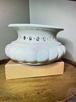 side view of white ceramic planter showing scalloped body and pierced rim