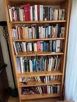 Full view of five-shelf pine bookcase filled with assorted books