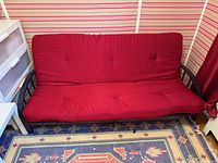 Front view of futon upright showing red cushion and black metal frame