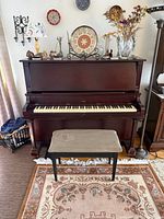 Front view of Evans upright piano with bench and decorative items on top