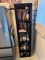Full view of shelf next to fridge showing cookbooks, mugs, travel cups