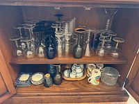 Cabinet view of entire lot showing stemware on upper shelf and mugs, plates, bowl on lower shelf