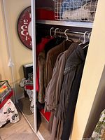 First closet section showing several coats including red, brown suede with fur, brown suede, taupe trench, taupe parka, black coat