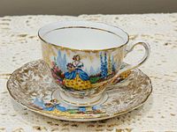 Teacup on saucer showing full pastoral scene and gold gilt detailing