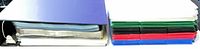 Binder laying on side showing stack of assorted coloured pocket pages inside and additional stack beside