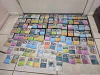 Wide shot of entire spread of roughly 100 Pokémon cards laid out on floor